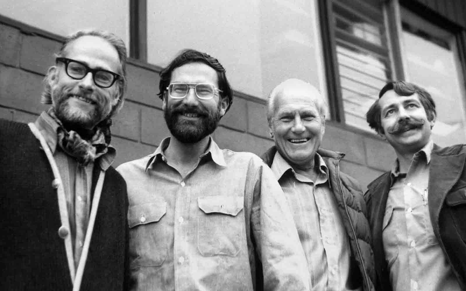 About Us: Four men with beards and glasses are posing for a photo.