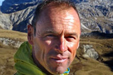 A man in a yellow jacket standing in front of mountains.
