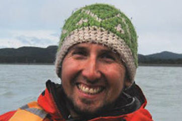 A smiling man wearing a knitted hat on a boat.