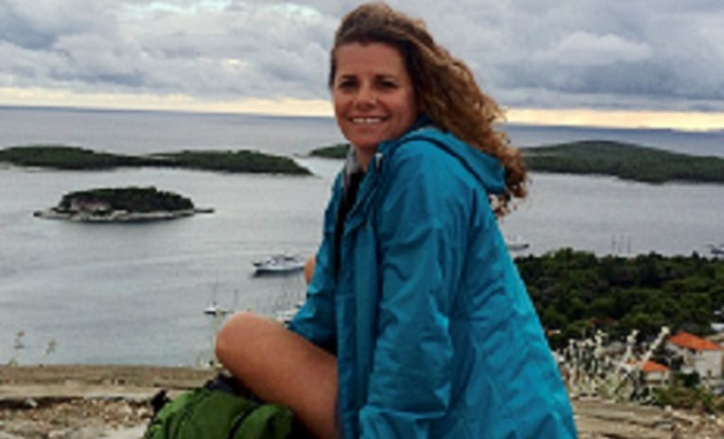 A woman in a blue jacket sitting on top of a mountain.