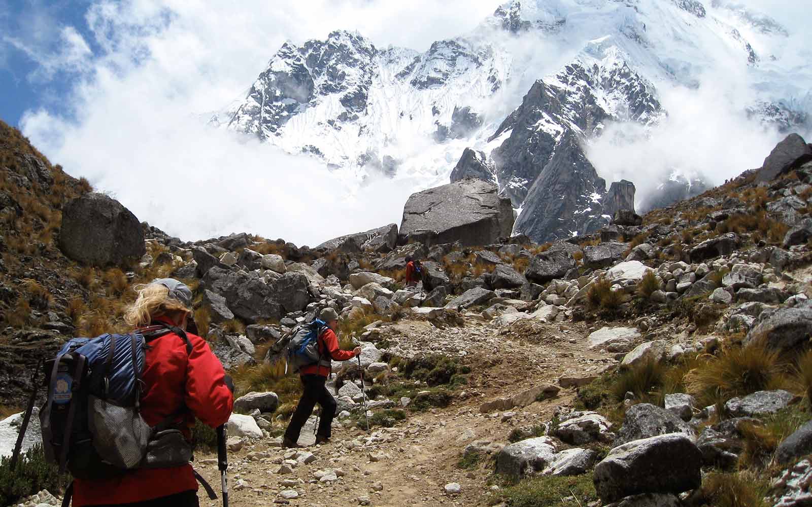 A group of people hiking up a rocky trail with mountains in the background.