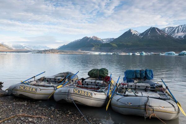 Three rafts on the shore of a body of water with mountains in the background.