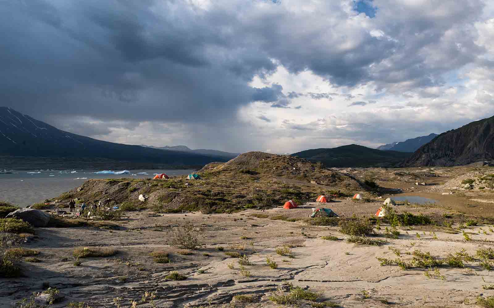 A group of tents set up near a lake and mountains.