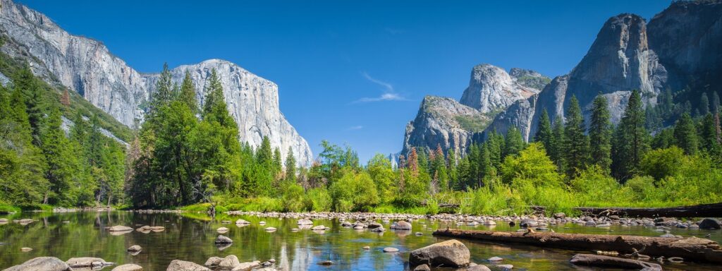 Classic view of scenic Yosemite Valley with famous El Capitan rock climbing summit and idyllic Merced river on a sunny day with blue sky and clouds in summer Yosemite National Park California USA.