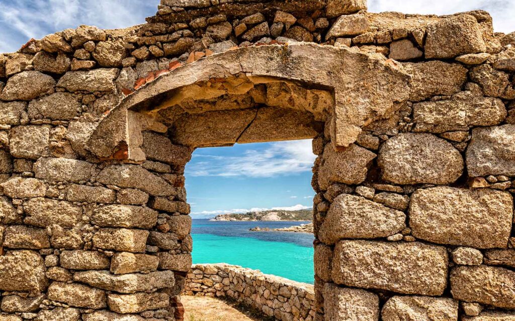 A stone arch structure on the hiking trail in Corsica, France with the Mediterranean Sea in the background.