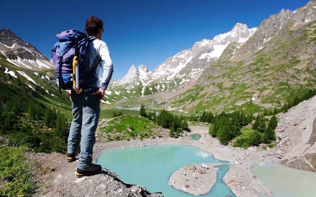 Man hiking in France on the Tour du Mont Blanc trail looking at a glacier mountain lake.