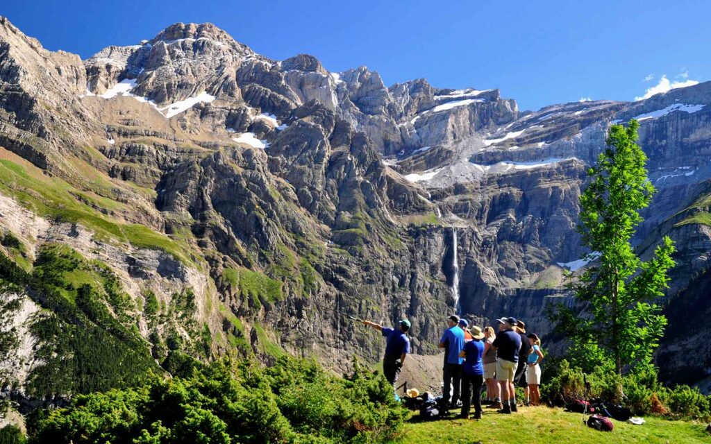 A group of people standing in front of a majestic mountain with a breathtaking waterfall, exploring one of the best hikes in France.