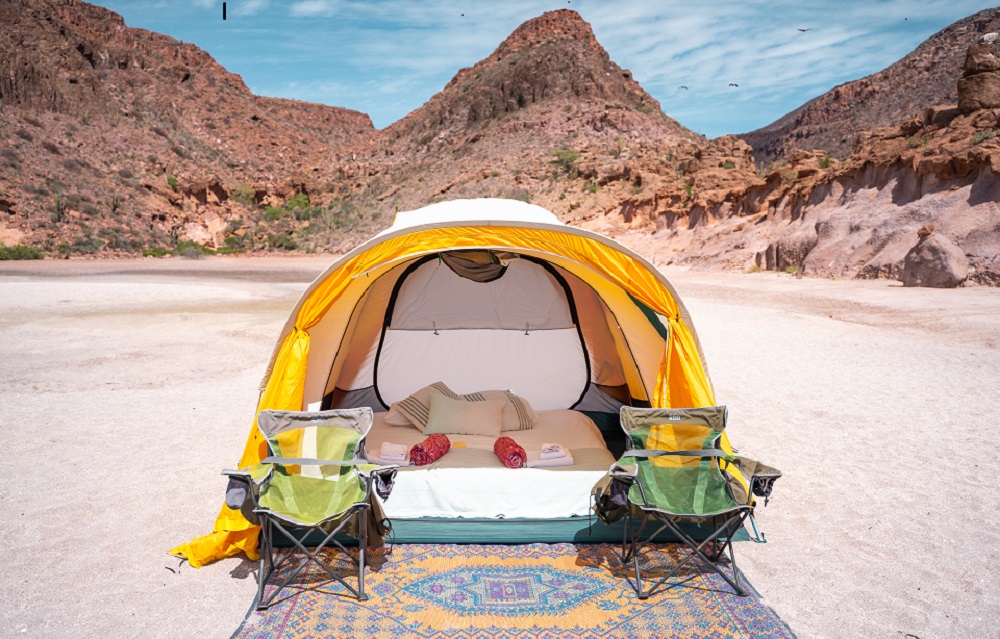 A tent set up in the desert with chairs and a rug.