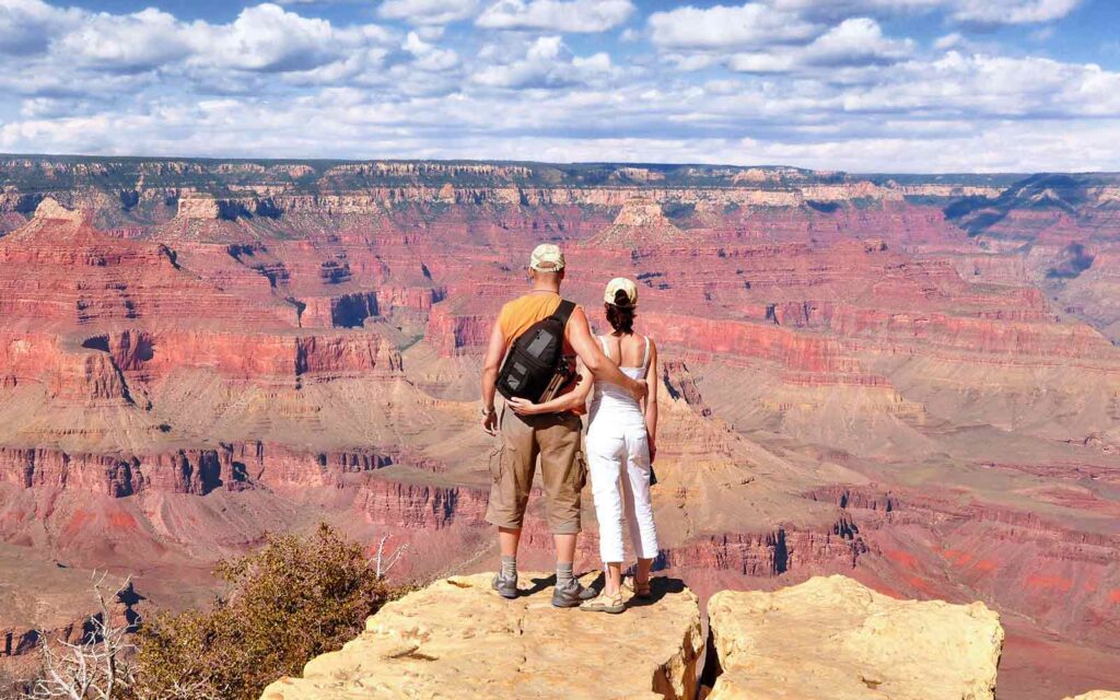 Two people standing on a cliff overlooking the grand canyon.