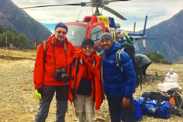 Three people standing in front of a Nepal Trekking helicopter.