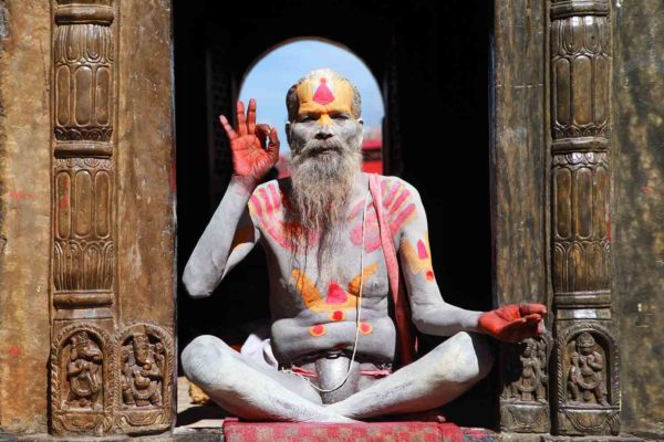 A man with a painted face sits in front of a door during his Nepal Trekking Adventure.