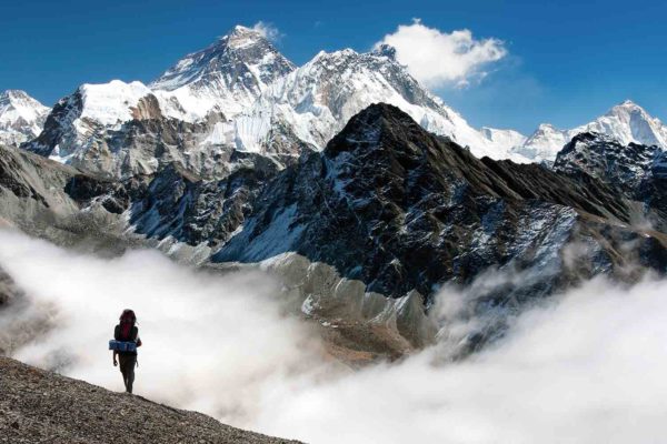 A person enjoying Nepal Trekking Adventures on top of a mountain with clouds in the background.
