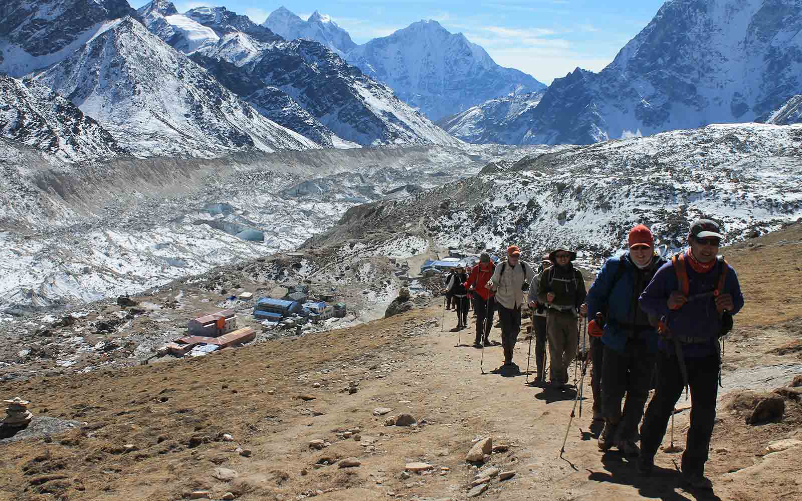 A group of people on a Nepal trekking adventure, hiking up a trail with mountains in the background.