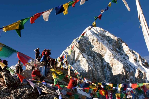 A group of people on a Nepal trekking adventure, standing on top of a mountain adorned with prayer flags.