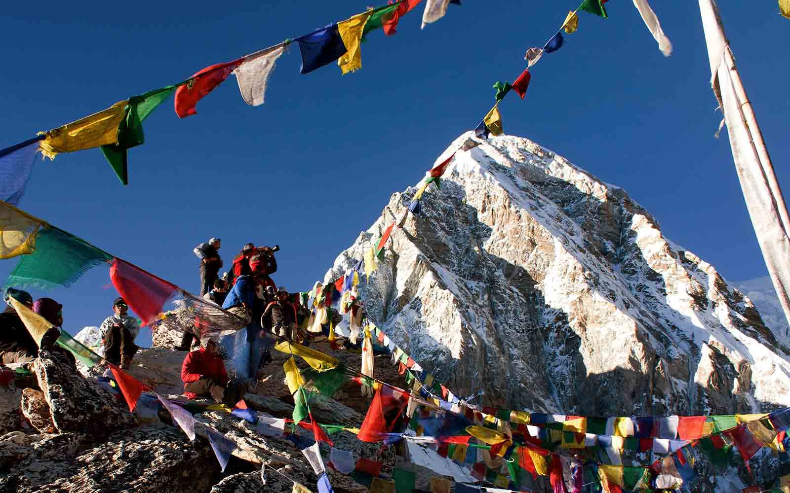 A group of people on a Nepal trekking adventure, standing on top of a mountain adorned with prayer flags.