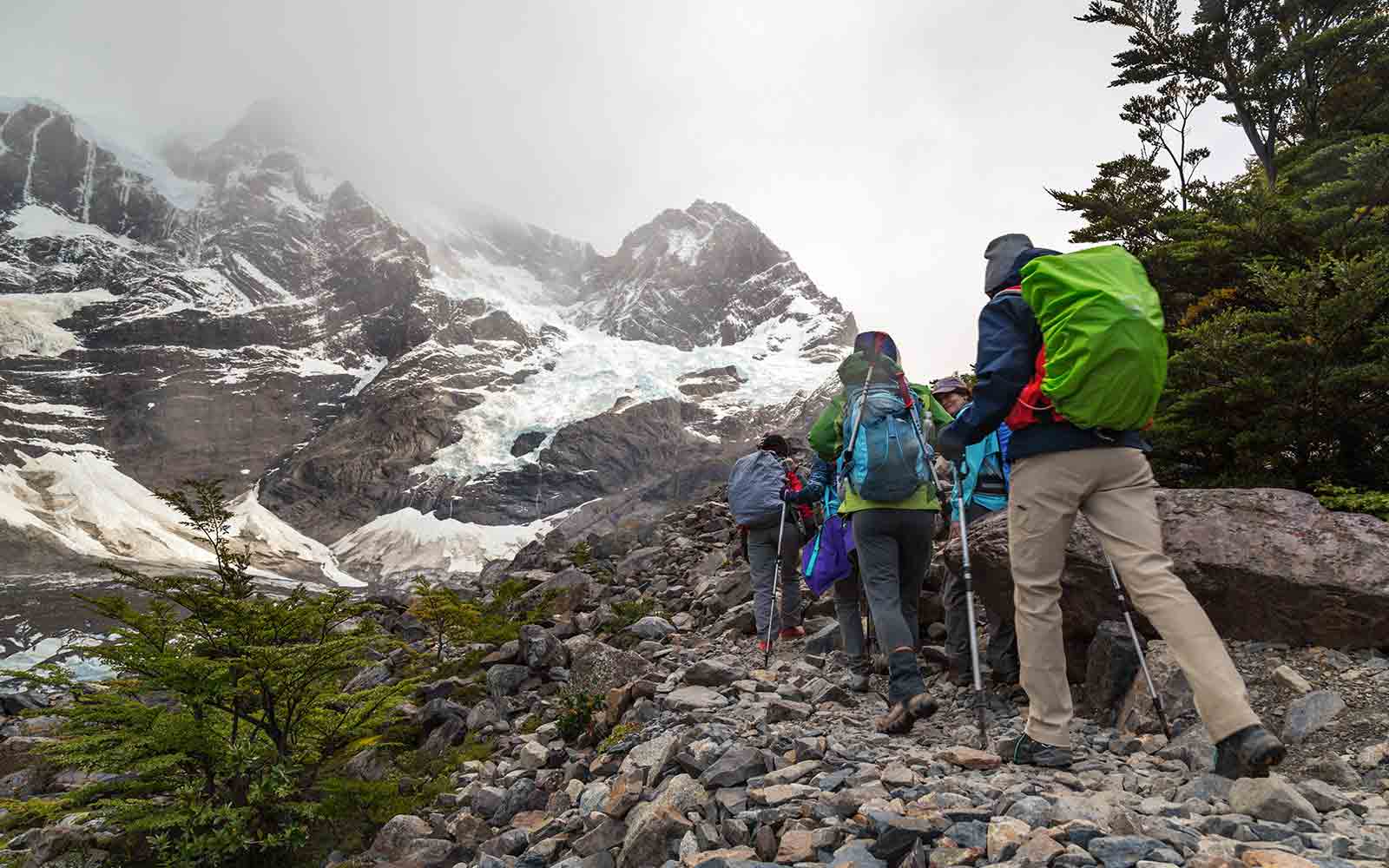 A group of people hiking up a rocky path near a snowy mountain, experiencing active adventures in Patagonia.