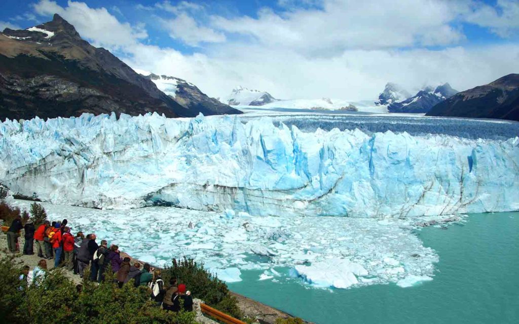 A group of people standing in front of a large glacier, experiencing one of the best adventures in Patagonia.