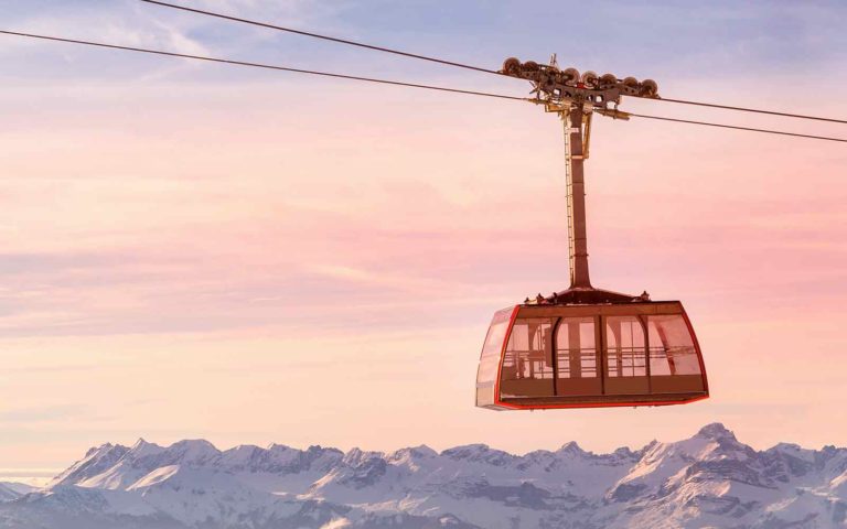 A cable car high up in the air with a beautiful view of the snowy Swiss Alps