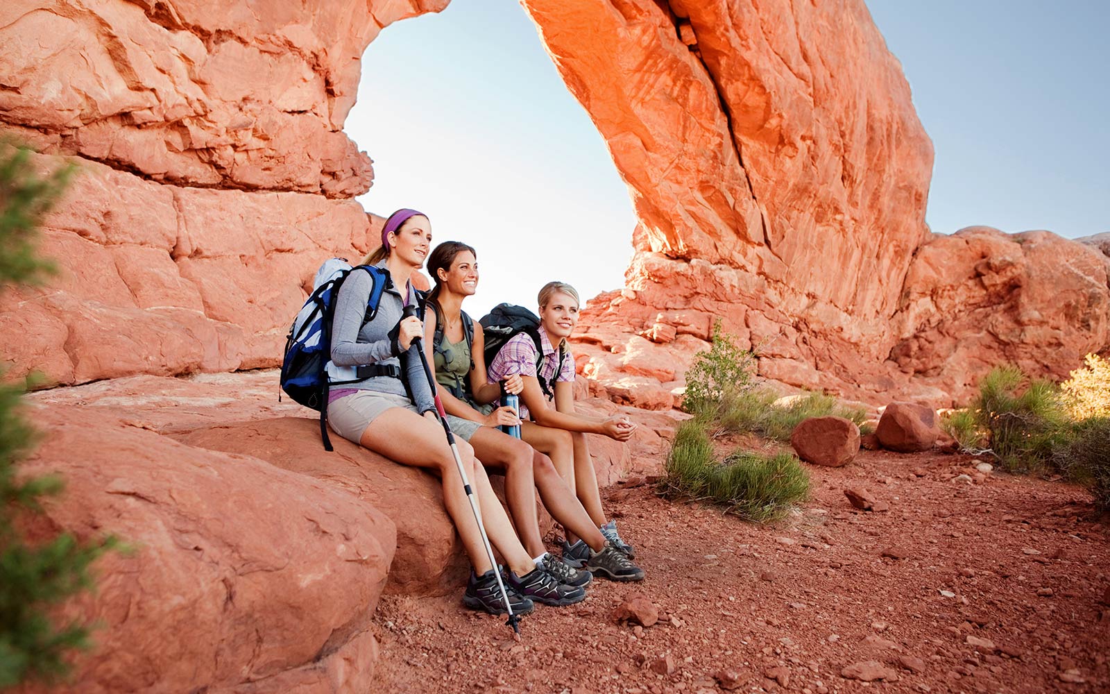 Three hikers sitting on a rock in Arches National Park, Utah during an adventurous USA tour.