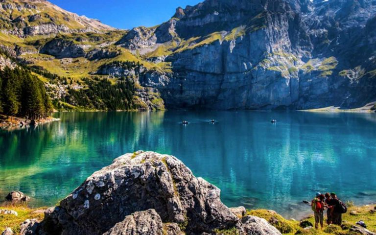Hikers looking at a beautiful crystal clear blue glacial like high up on the Chindbetti Pass in the Alps