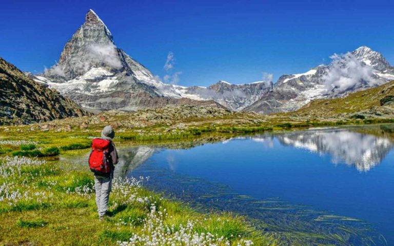A hiker on a high altitude trail looking at a breathtaking view of the Matterhorn