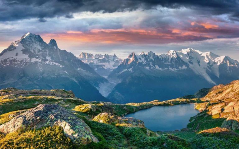 A gorgeous view of a pristine mountain lake surrounded by grassy meadows with the Alps in the background