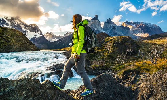 A woman in a green jacket is standing on a rock next to a river.