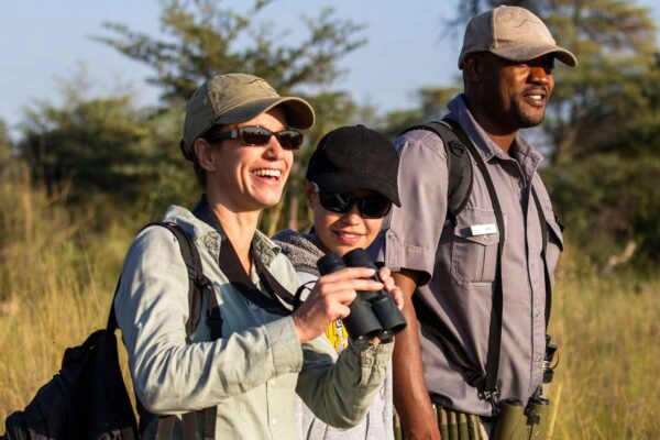 Three people with binoculars standing in an African field, embarking on an adventure travel.