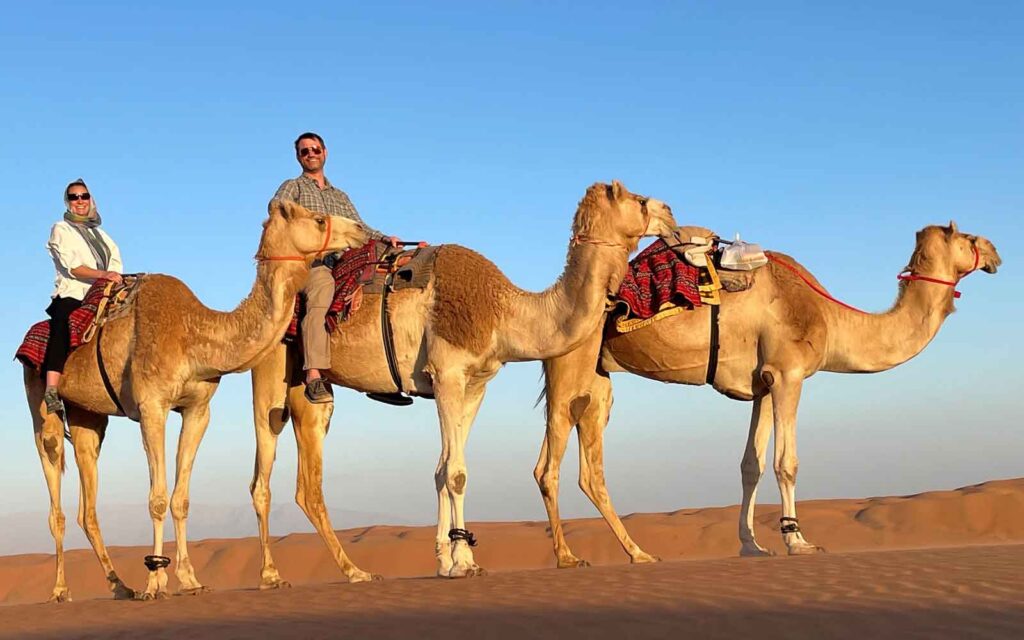 Three people riding camels in the desert.