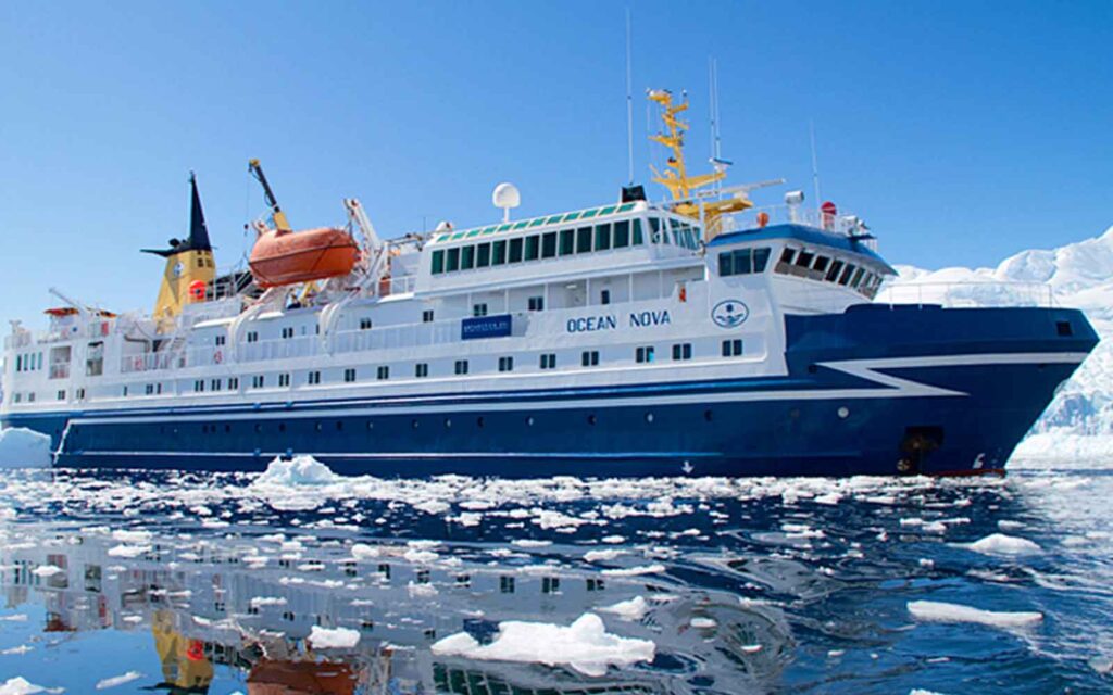 A polar cruise ship is floating near icebergs in the water.