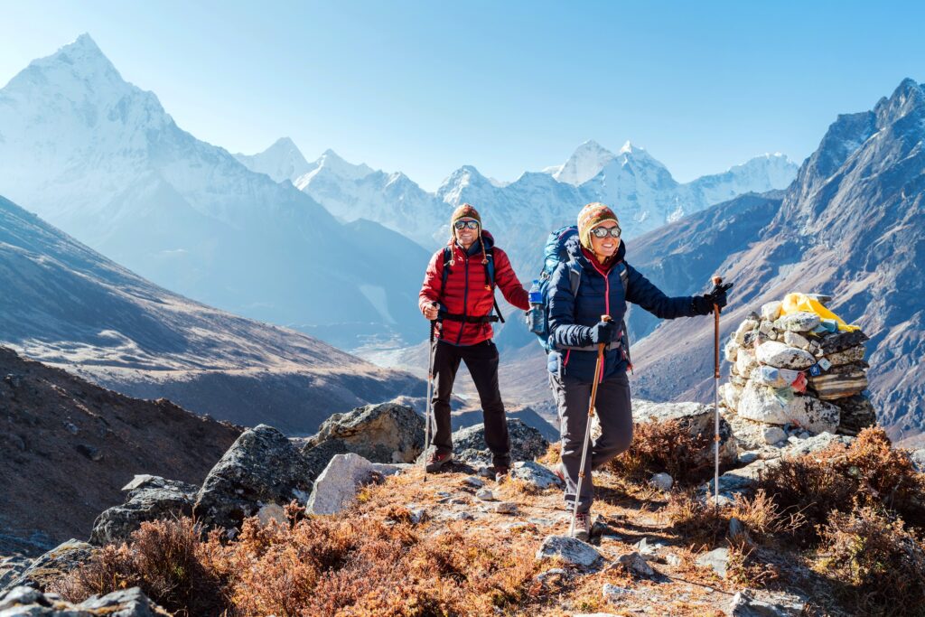 Couple following Everest Base Camp trekking route near Dughla 4620m. Backpackers carrying Backpacks and using trekking poles and enjoying valley view with Ama Dablam 6812m peak