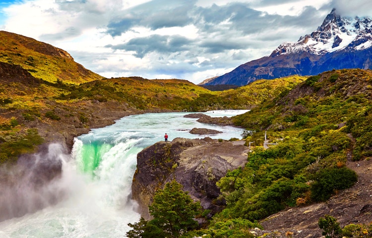 solo hiker female standing very close to a giant waterfall in Argentina in Torres del Paines