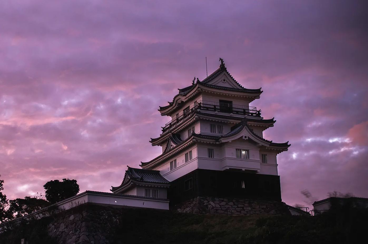A castle sits on top of a hill under a purple sky in Japan.