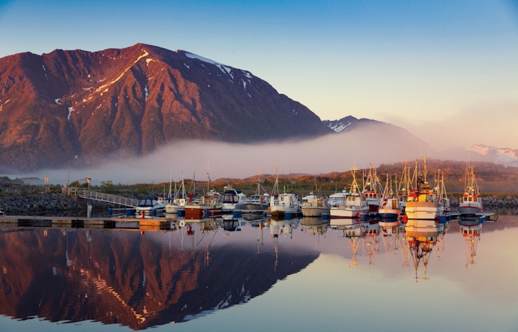 Norway: Boats docked in a harbor with mountains in the background travel guide.