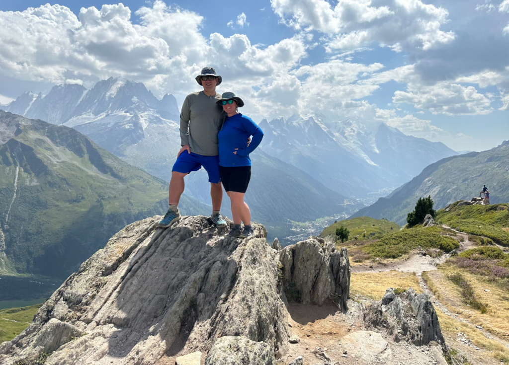 Two people standing on top of a mountain with mountains in the background.