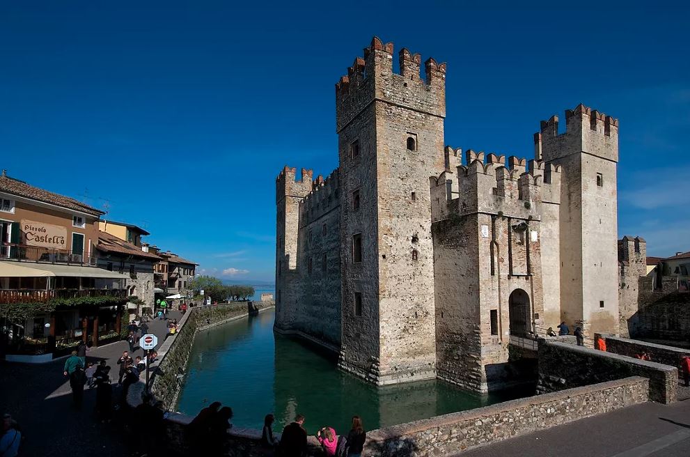 A castle on a river with people walking around it.