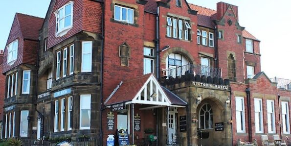A large, red-brick Victorian-style hotel with white trim and multiple windows; signs read "Victoria Hotel" and "Garfunkel's Restaurant.