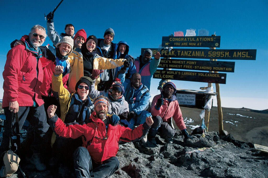 Group of hikers hugging in front of a sign at the summit of Mount KIlimanjaro in Tanzania
