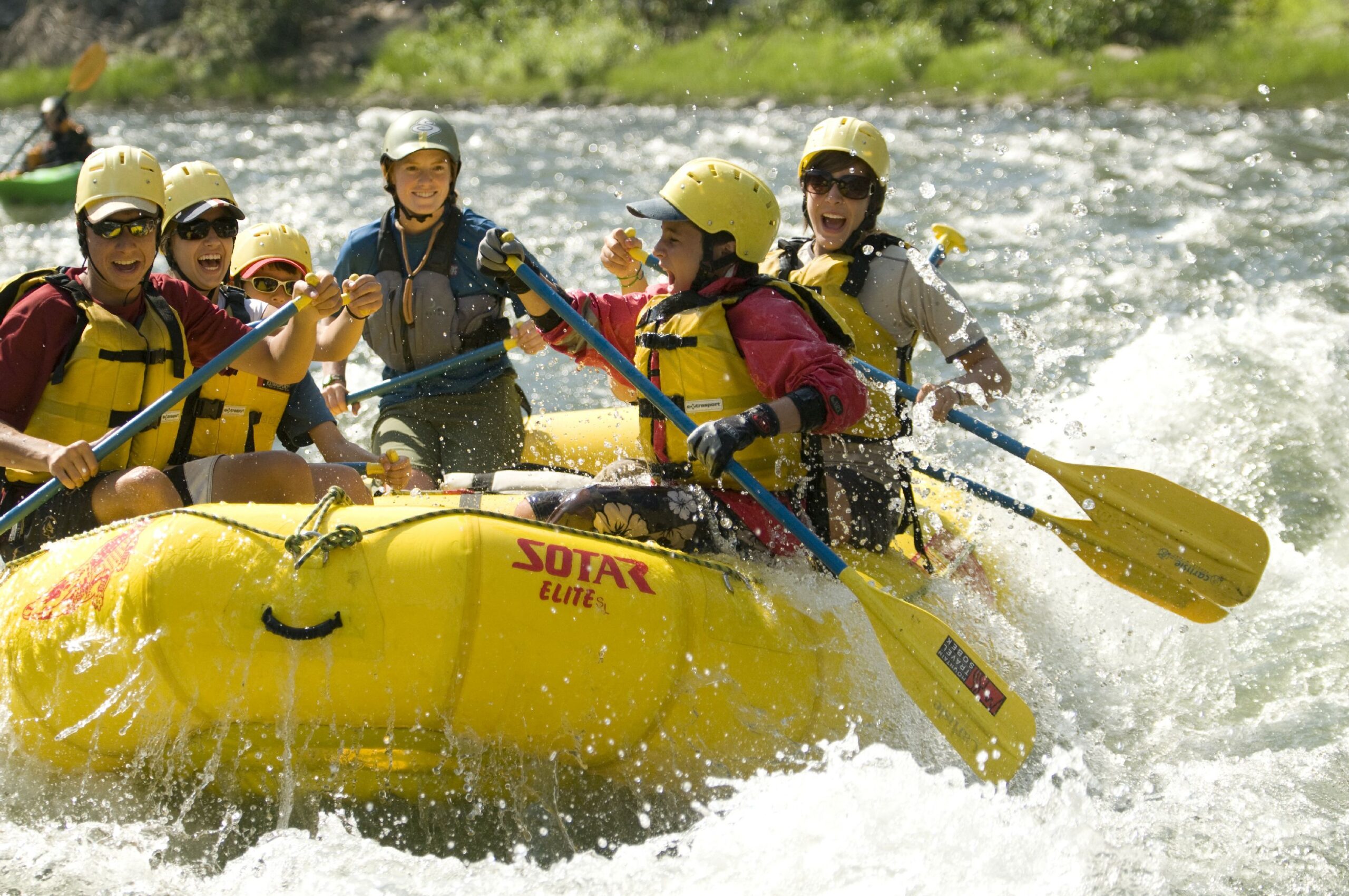 A group of people wearing helmets and life jackets paddle a yellow raft through whitewater rapids on an exciting Idaho River Rafting adventure.