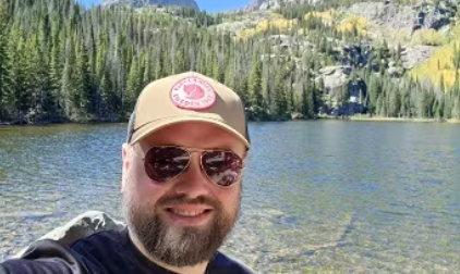 male man with hat beside a clear blue lake in natural surroundings in spring