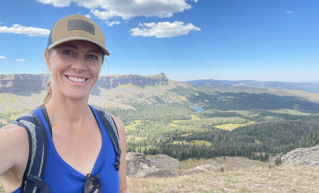 a woman hiker smiling in front of panoramic views on hike in North America