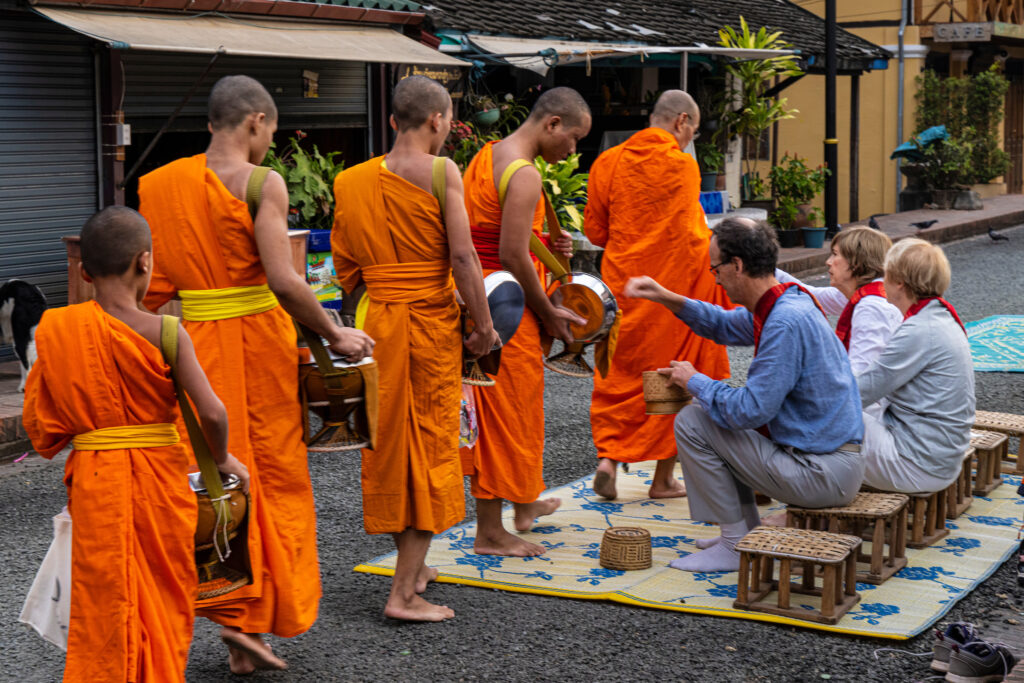 travelers practicing alms giving, a practice, in Laos, to visiting Buddhist monks in bustling town of Laos, Asia