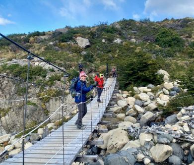 Diane on a hiking trail to Paso Los Cuernos trail on a suspension bridge near a river stream in Patagonia