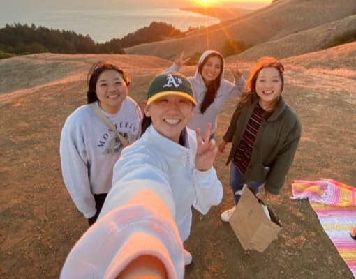 Four people pose for a selfie on a hilltop at sunset with a scenic view of the ocean in the Bay Area and landscape in the background.
