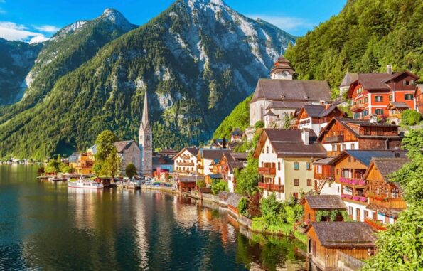 A picturesque lakeside village with colorful houses, a church with a tall steeple, and lush green mountains in the background in Austrian Alps