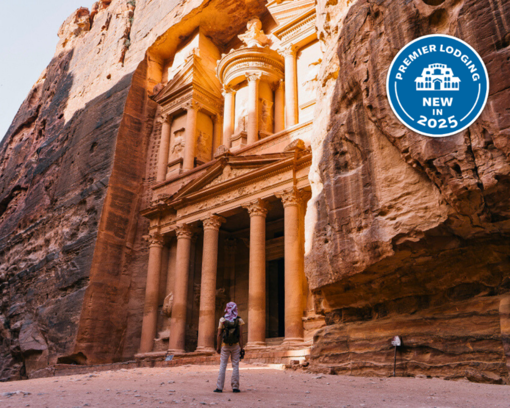 A person stands in front of the ancient rock-cut architecture of Petra in the Middle East, with a "Premier Lodging New in 2025" badge