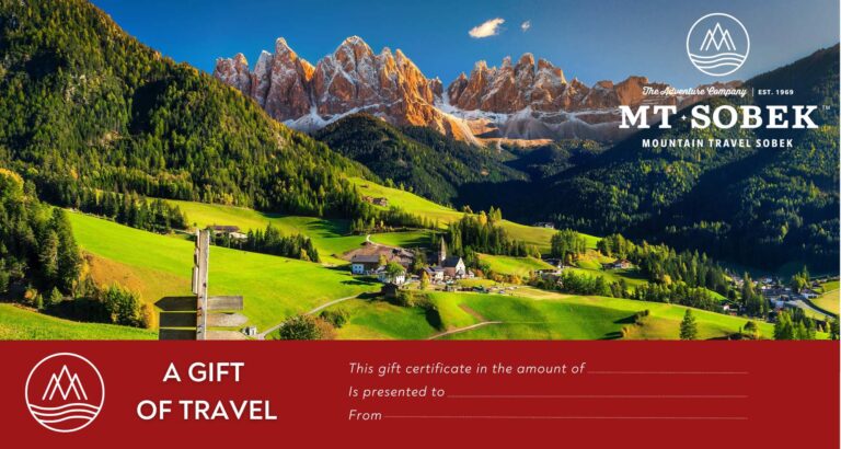 Gift certificate for Mt Sobek featuring a scenic mountain landscape with a village, green fields, and dramatic rocky peaks under a clear blue sky—a perfect gift for adventurers.