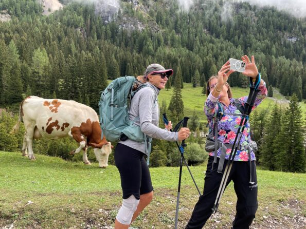 hikers in the Dolomites in the valley taking a photo with a cow