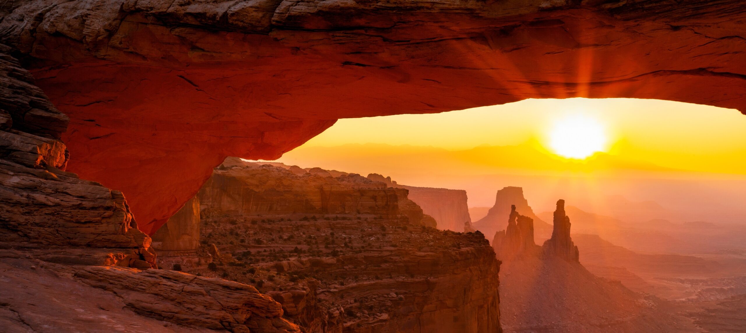 The sun rises over sandstone rock formations, viewed through the Mesa Arch in Canyonlands National Park—a stunning highlight of Utah national parks hiking adventures.