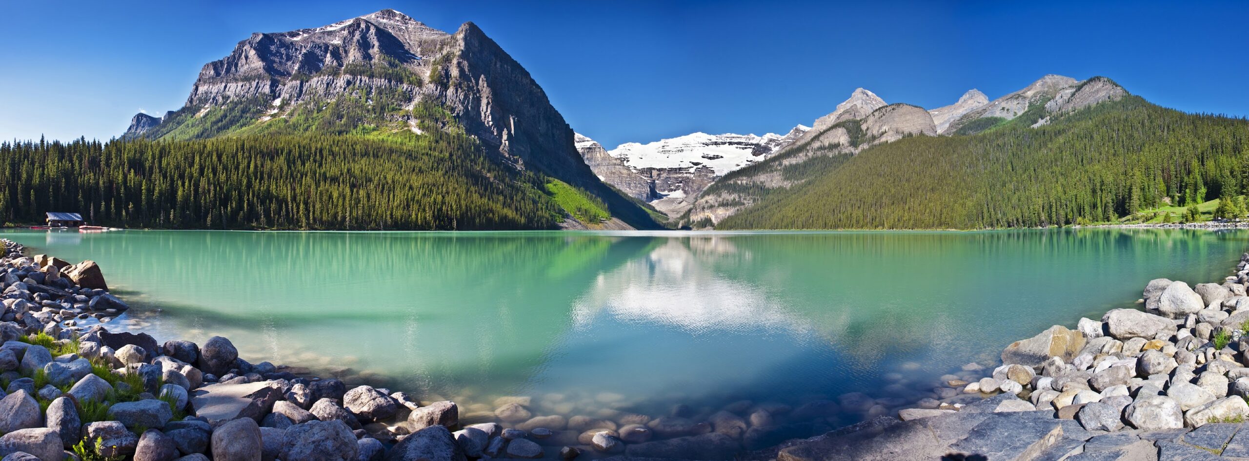 Turquoise lake with rocky shore, surrounded by pine forests and snow-capped mountains under a clear blue sky—an unforgettable scene on the best Canadian Rockies hiking tours.